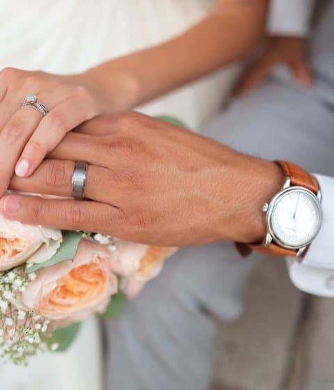 A couple's hands with their rings over a bouquet